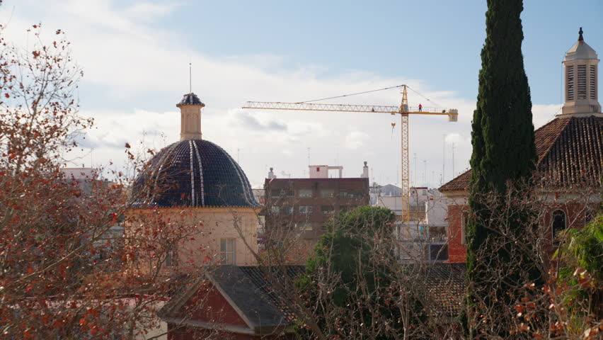 Historic buildings and modern construction crane creating a contrast in the urban landscape under a cloudy sky.