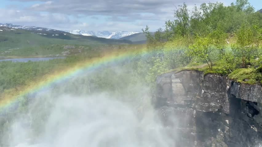 Luminous rainbow extends across peaceful river scene. Colorful rainbow arches across serene waterfall surrounded by rolling hills