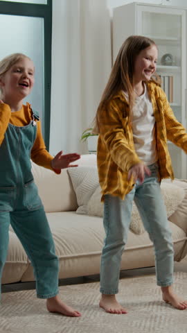 Two joyful Caucasian sisters children friends smile dancing moving to song activity siblings kids girls daughter dance smiling listening music family joy weekend in living room at home happy childhood