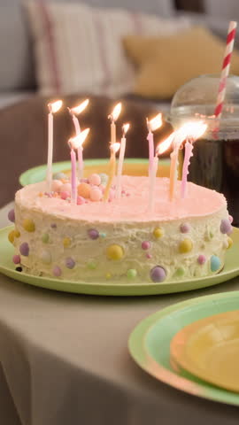 Vertical shot of fancy round cake with lit multicolored candles and Caucasian girl blowing them out during birthday celebration