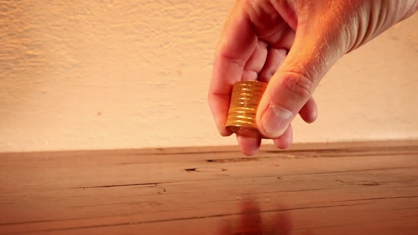 Close-up on hand counting stacked gold coins on wood tabletop, wealth concept