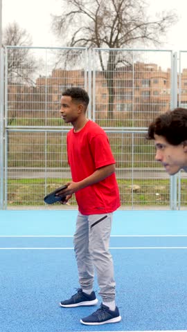 Two athletic friends playing a competitive game of pickleball on a vibrant blue outdoor court, one player celebrates after scoring the winning point against his opponent in a friendly match