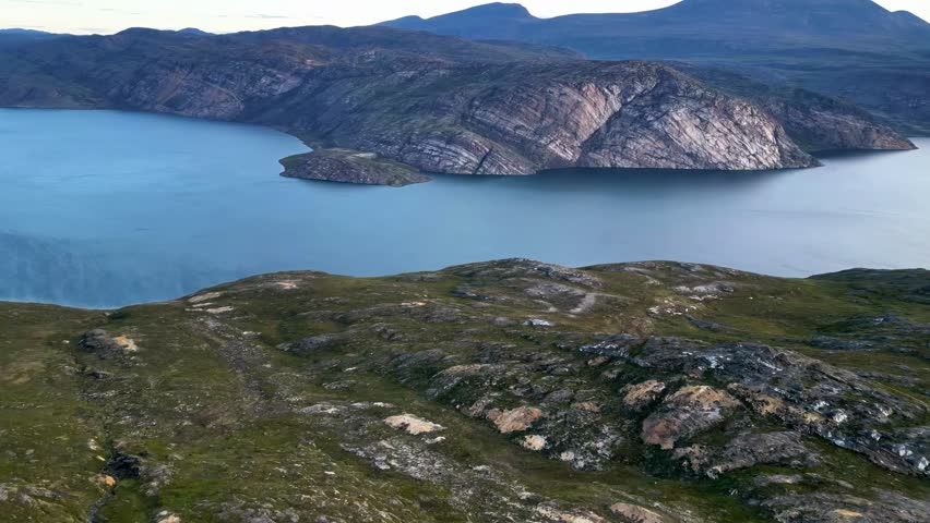 A breathtaking aerial view of a serene Greenlandic fjord, showcasing dramatic rocky coastlines and the vast expanse of the Arctic ocean