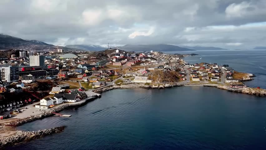 Aerial view of Nuuk, the capital of Greenland, showcasing a mix of traditional and modern architecture along the coast under a cloudy sky