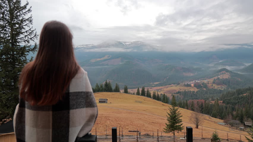 Back view of woman looking at misty peaks, girl wrapped in blanket on balcony