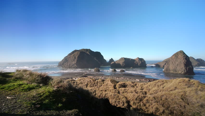 A person stands on a coastal cliff overlooking sea stacks and waves along the Oregon Coast, capturing a wide Pacific Ocean view with rugged shoreline, open sky, and calm natural atmosphere