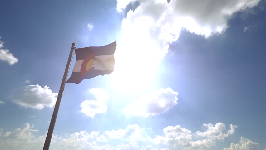 Colorado State Flag (USA) waving on a Flagpole from a Moving Angle in front of a blue sky with clouds
