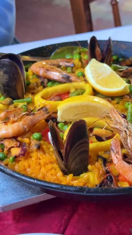 Traditional Spanish seafood paella with prawns mussels and lemon slices in a large frying pan, vertical video