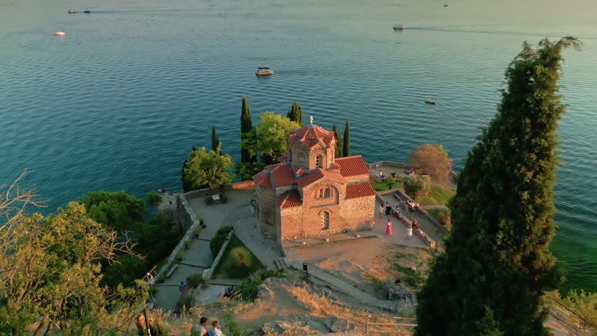 Aerial drone footage of the Church of St. John at Kaneo overlooking Lake Ohrid in North Macedonia. Scenic view of the iconic cliffside church, crystal clear water, historic architecture and dramatic coastline. Popular travel destination, UNESCO World Heritage site, peaceful spiritual landmark, cinematic summer landscape.