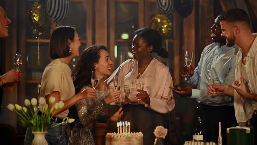 Group of multicultural friends celebrating a birthday. Happy young woman making a wish and blowing out candles on her cake at the party