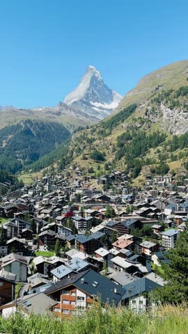 A breathtaking panoramic view of the iconic Matterhorn rising above the village of Zermatt, Switzerland, seen from the scenic Mürini viewpoint (Le Petit Village). The classic alpine peak dominates the skyline with crisp snow-capped ridges and dramatic lighting, framed by traditional chalets and lush alpine surroundings. This popular photo spot is reached by a short uphill walk from Zermatt and offers unobstructed, postcard-worthy perspectives of the Matterhorn against vivid blue skies — perfect for travel, landscape, and outdoor adventure imagery.