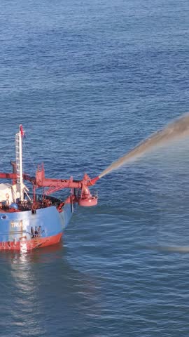 High-angle vertical shot of a ship spraying a powerful sand stream into the sea.