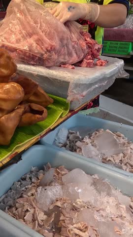 A vendor wearing gloves arranges fresh raw meat and offal at a traditional market stall.