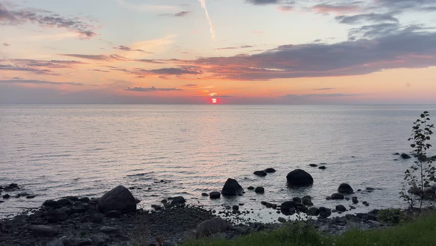 Golden sunset over Grand Beach on Lake Winnipeg with calm water and rocky shoreline under colorful evening sky.