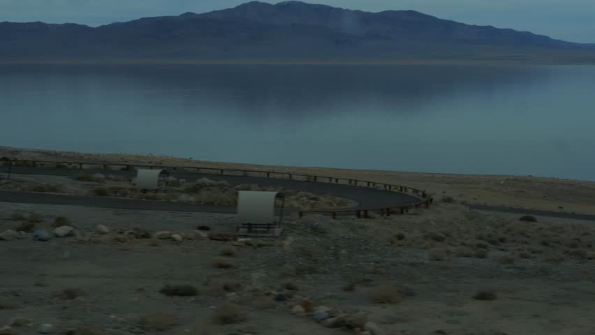 Pyramid Lake in Nevada with iconic tufa rock formations on desert shore, calm turquoise waters reflecting distant blue mountains under hazy sky, concept of remote natural beauty and serenity