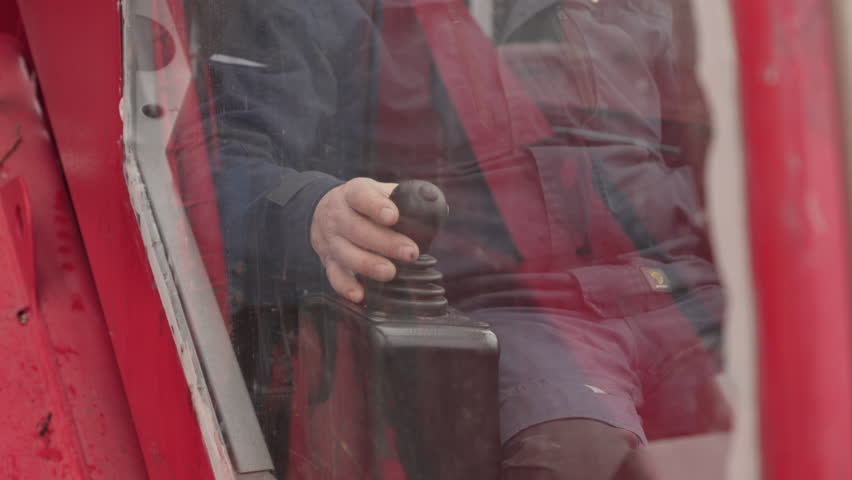 A man operates red heavy machinery, observing a snowy construction site