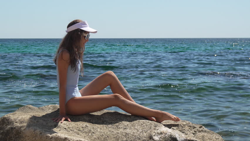 Woman, swimsuit, beach, young girl relaxing on rock by the blue sea on a sunny summer day