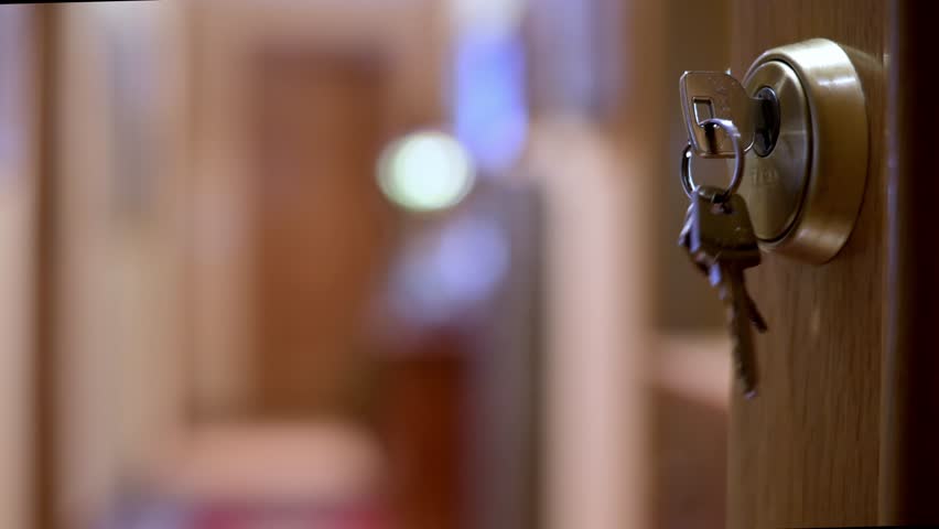 A closeup shot of keys on a keyring in a door lock, set in a warm hallway. It conveys home security, entry, safety, and everyday life moments.