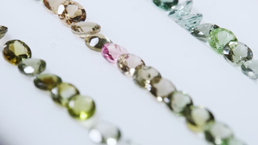 Rows of small colorful gemstones on white background.