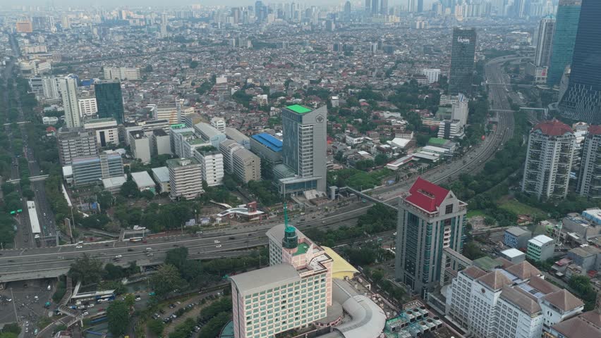 Wide aerial shot revealing the sprawling urban landscape of jakarta, indonesia, with modern skyscrapers, dense housing, and busy highway traffic