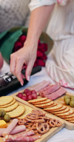 Love, picnic and hands of couple with food on blanket for bonding, relationship and flowers outdoor. Dating, weekend and people with charcuterie board for romance, anniversary and valentines day