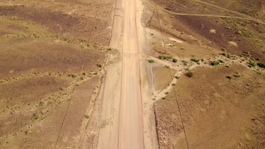 Aerial tilt-up reveal from a dirt road to a vast desert mountain panorama under a dramatic sky, Namibia.