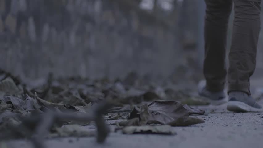 Low angle shot of man walking on footpath with digital camera in hand.