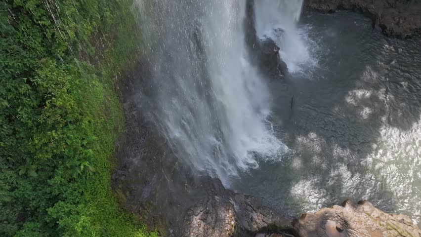Close aerial view of powerful waterfall pouring beside dense green cliff face.