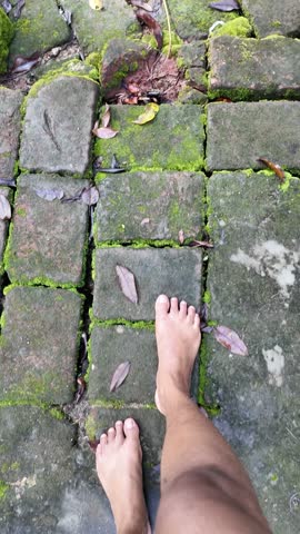 Barefoot walking on a moss-covered stone pathway surrounded by nature. Slow mindful movement symbolizing grounding, calmness, and a deep connection with the earth.