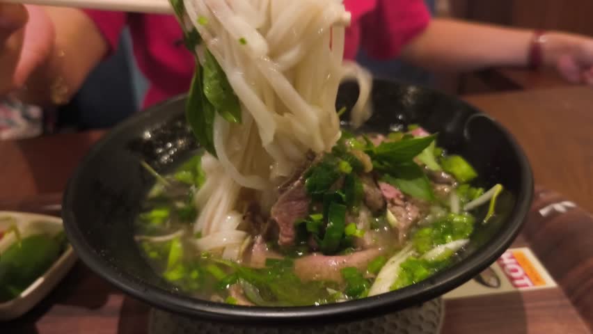A bowl of Pho or Vietnamese beef noodle soup with chopsticks, served on a wooden tray with a rich and savory broth.