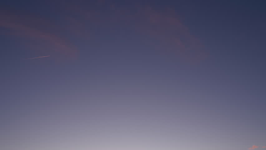 Horizontal view of a tranquil evening sky transitioning from deep blue to warm tones. A distant airplane and wispy clouds add subtle movement to the peaceful atmosphere