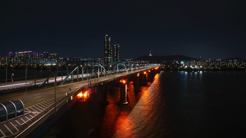 Night timelapse of traffic light trails on Dongjak Bridge crossing the Han River with N Seoul Tower in the background. Dynamic aerial cityscape of Seoul, South Korea showcasing urban transportation, illuminated skyline and modern infrastructure.