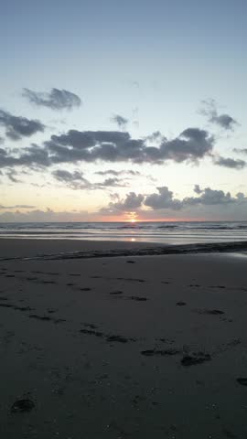 Serene sunrise over ocean horizon with dramatic clouds, gentle waves, and wet sand reflecting pastel sky, minimalist seascape background with copy space.