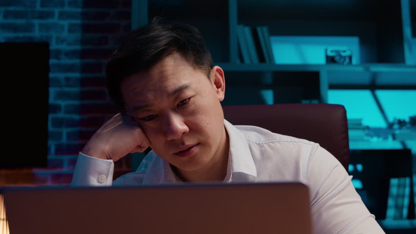 Unhappy Asian 40s business man looking in laptop at night Korean businessman sad with failure work difficulty problem sleepy Japanese male Chinese specialist computer overworked tired late at evening