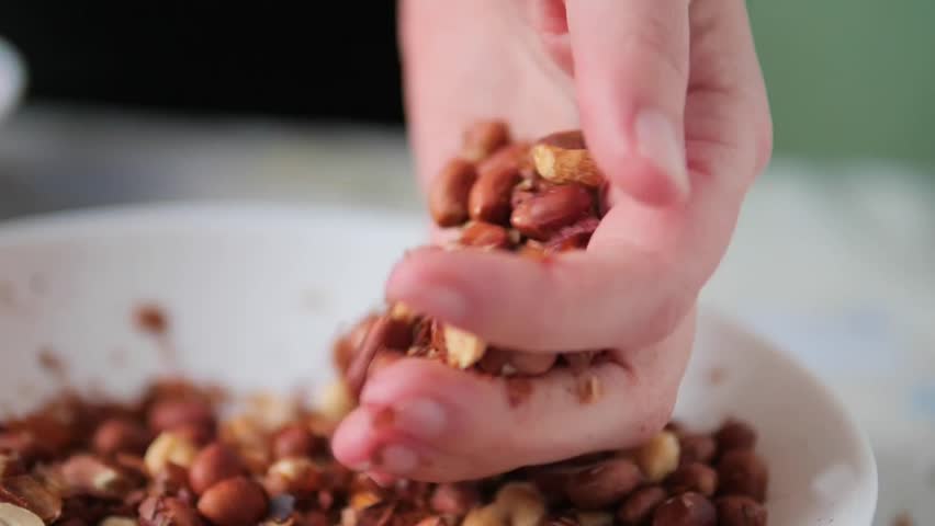 hand holding a large scoop of roasted peanuts above a white bowl - handful of freshly roasted peanuts and loose skins being gathered and sorted
