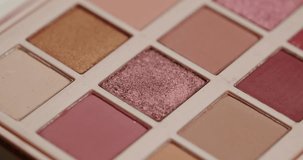 Close-up slow motion shot of a professional makeup artist's brush gathering sparkling pink and rose gold eyeshadow from a colorful palette, showing the texture and pigment of the cosmetic - Powered by Shutterstock - Get 15% off with code: PIKWIZARD15