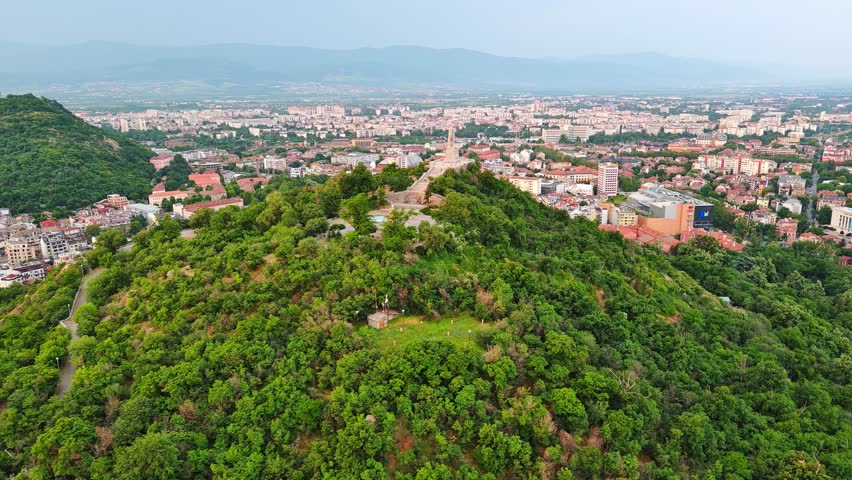 Town Plovdiv with houses and fields against backdrop of Rhodope Mountains and hills covered with forests and cloudy sky