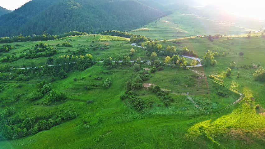 A road passes hills covered with spruce forests and meadows against a cloudy sky