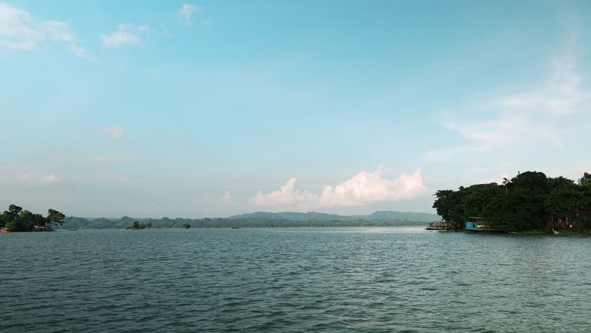 Wide scenic view of beautiful Kaptai Lake with blue water hills and clouds presenting peaceful natural landscape.