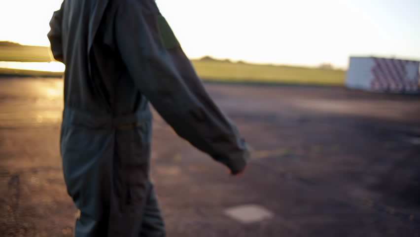 Military Pilot Walking on Air Base Runway Holding Helmet at Sunrise, Low Angle Detail - 4K