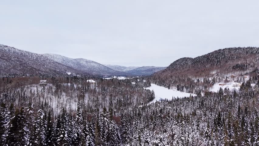 Wide aerial winter view of forest mountains and river in Canada.