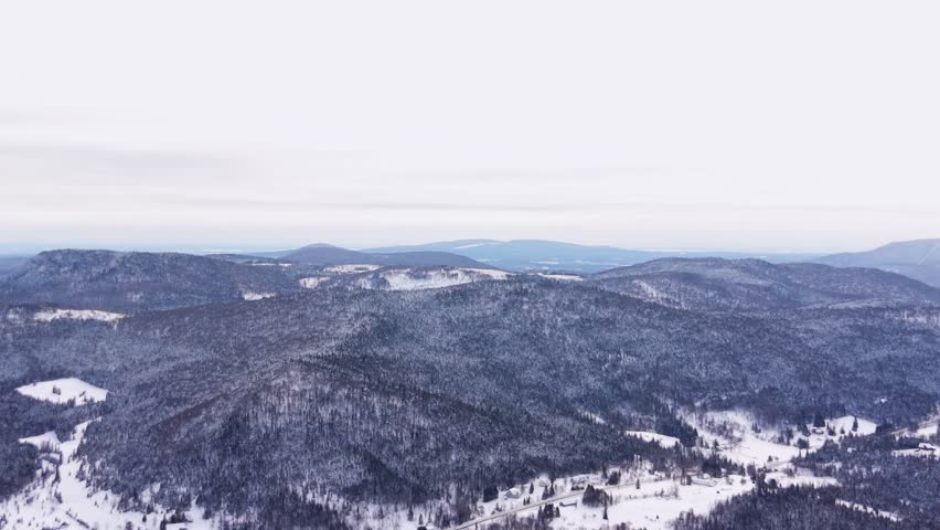 Aerial winter scenery of forested mountains in Canada with river near road.