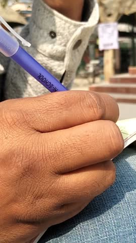 Close-Up of Hand Writing on Paper with Pen in Public Place