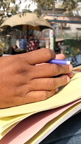 Close-Up of Hand Writing on Paper with Pen in Public Place