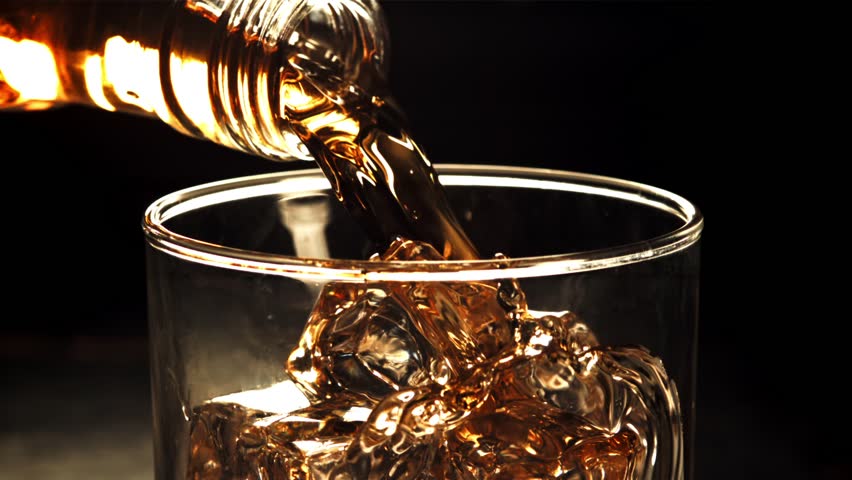 Golden whiskey is poured over ice in a glass, capturing a refreshing beverage, bar scene, and elegant drinking experience.