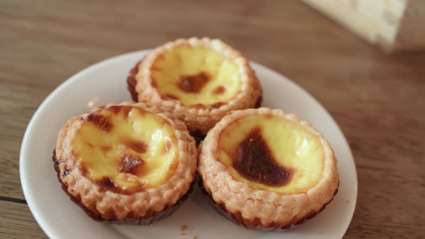 Three small egg tarts pastry served on a white plate, featuring a golden, caramelized custard filling.