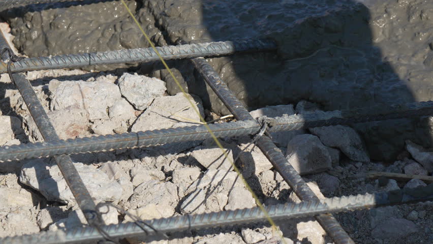 Concrete pouring construction site rebar, wet mixture flowing over rocks and metal bars, laying building foundations