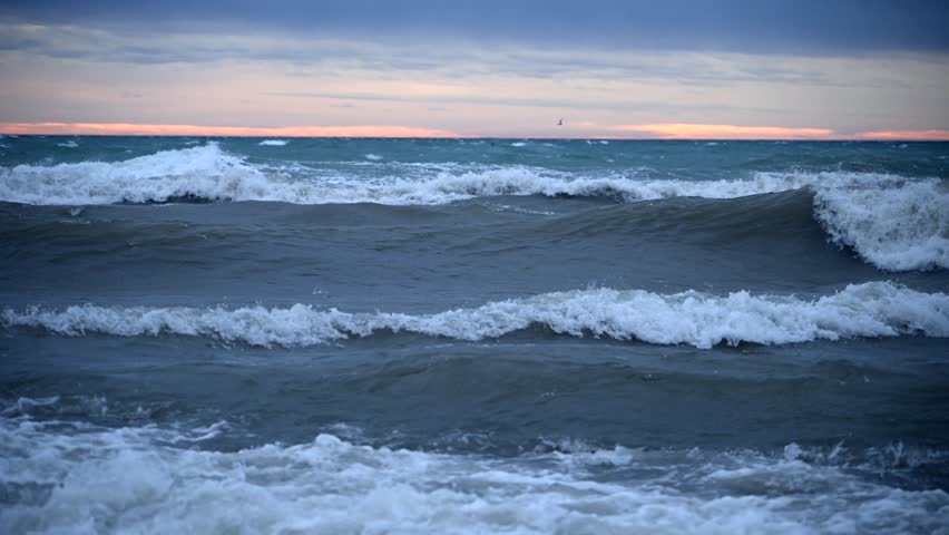 Waves Crash on the Shore as Storm Clouds Gather Over the Ocean During Sunset in Slow Motion