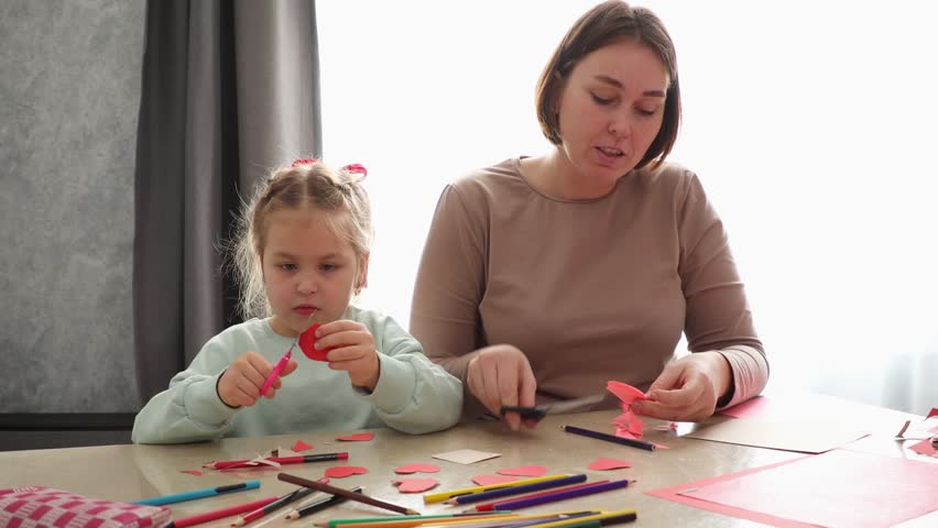 Portrait of Caucasian young woman and a cute little girl are carving and making crafts for the holiday together, sitting at a table. Pre-school children