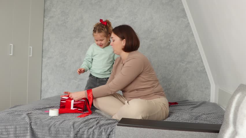 Wide shot of young mother and a little daughter pack gifts together for Valentine